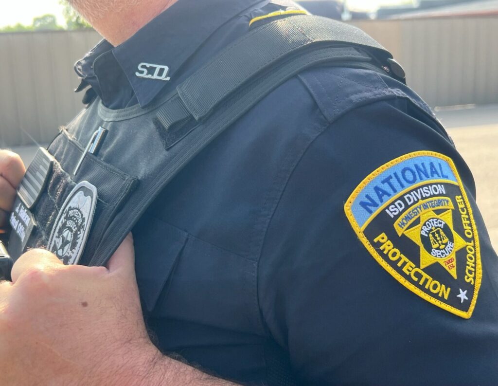 A person wearing a school officer uniform with a visible "National Protection" badge on the sleeve.